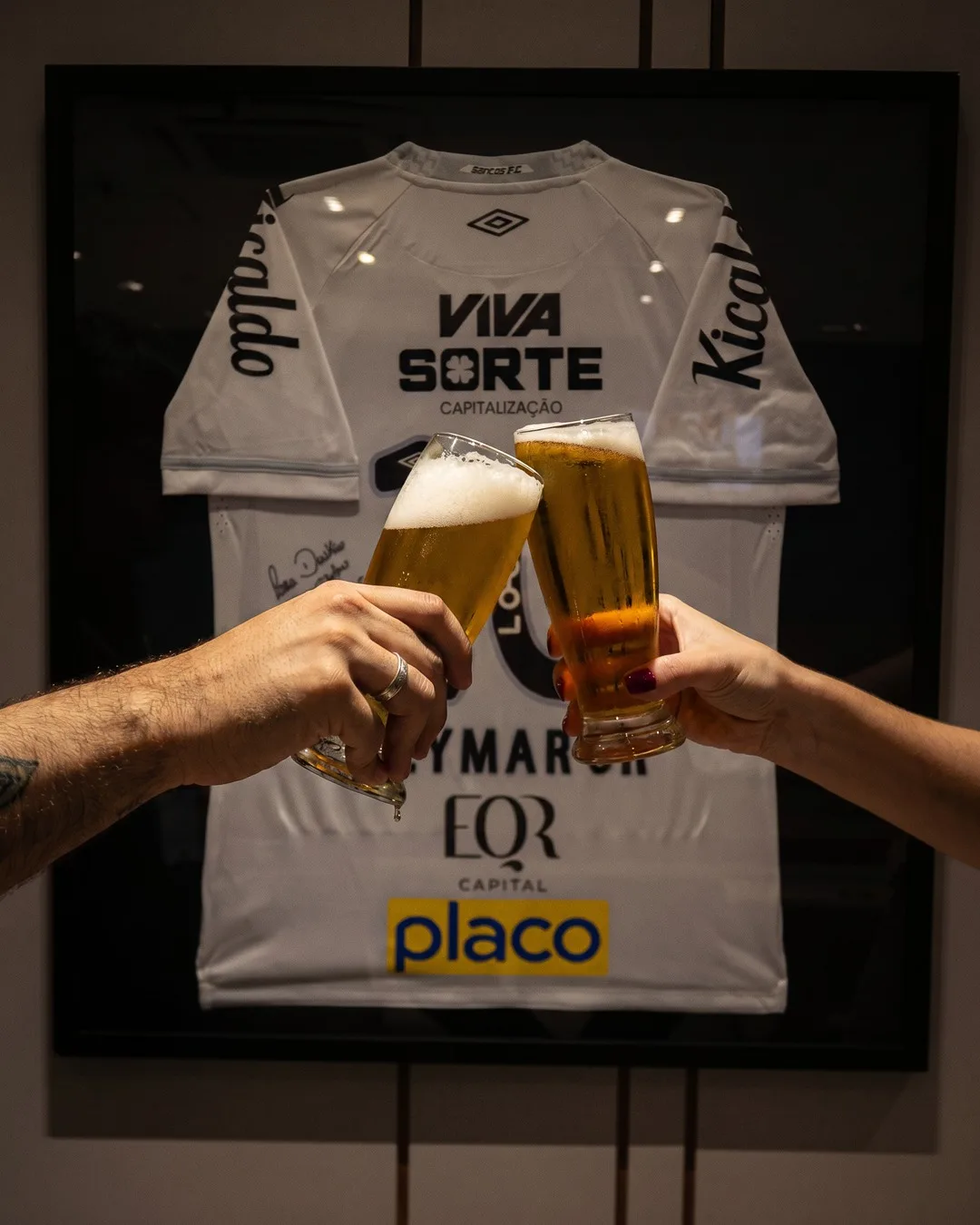 Brinde com chope gelado em frente à camisa oficial emoldurada